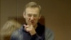RUSSIA -- Russian opposition leader Aleksei Navalny, charged with defaming a World War II veteran, gestures from inside a glass cell during a court hearing in Moscow, February 16, 2021